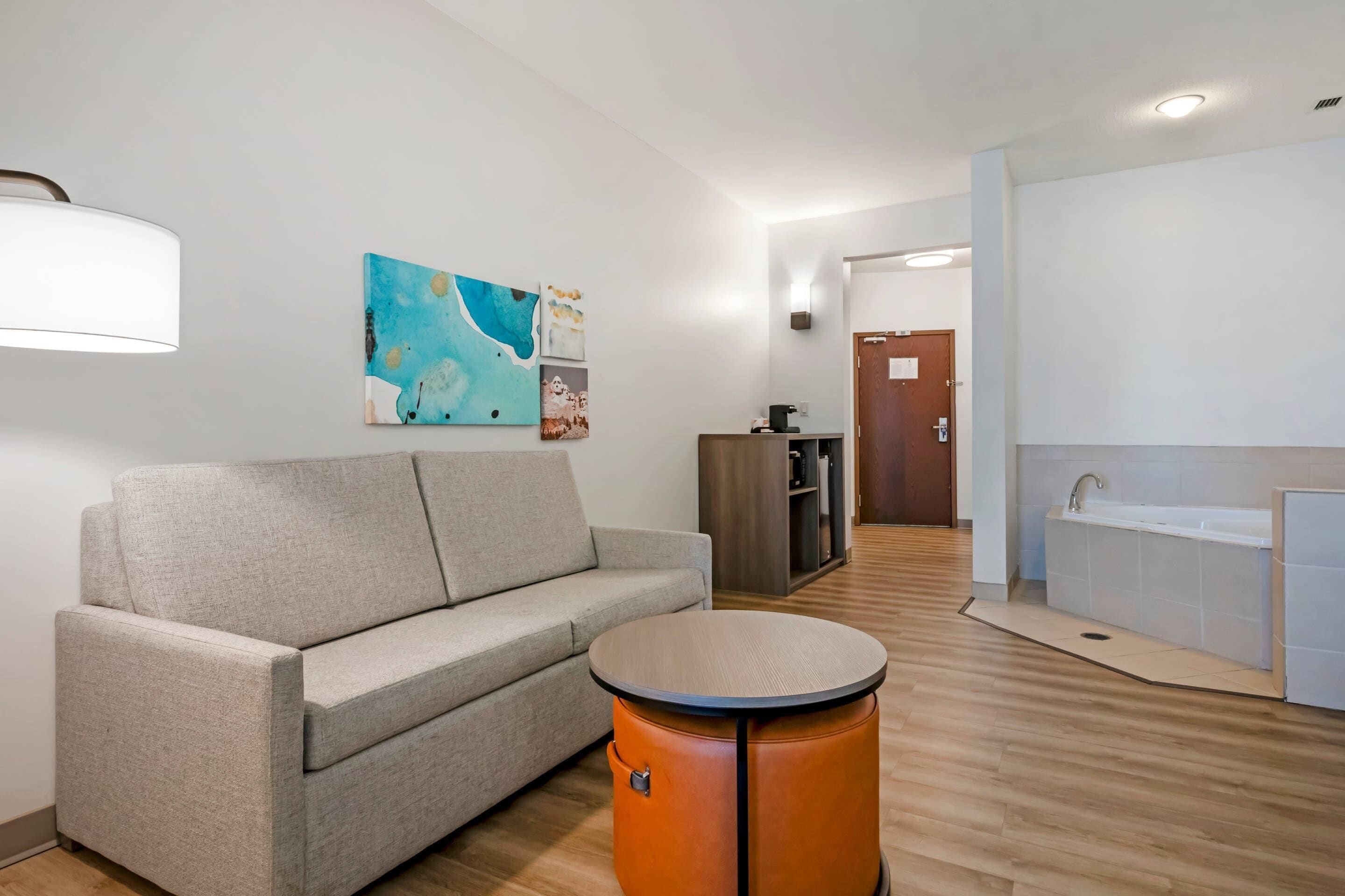 A modern interior with a sofa, a round table, a painting, a cabinet, and a kitchen area.