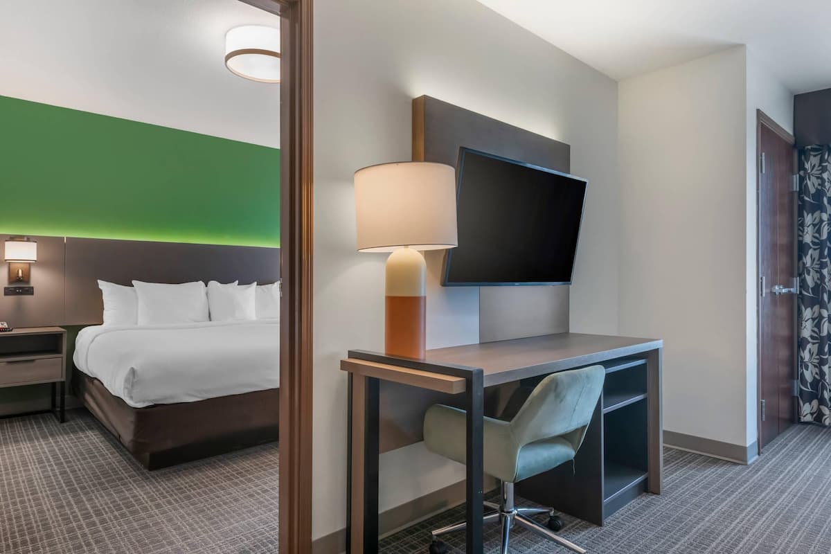 A hotel room with a bed, desk, chair, lamp, TV, and a green accent wall.