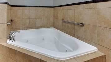 A white bathtub with a handheld showerhead and a grab bar, set against beige tiled walls with a black trim.