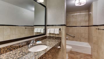 Un baño con lavamanos de granito, espejo, inodoro y bañera.