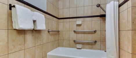 A bathroom with a bathtub, handrails, and a towel rack.