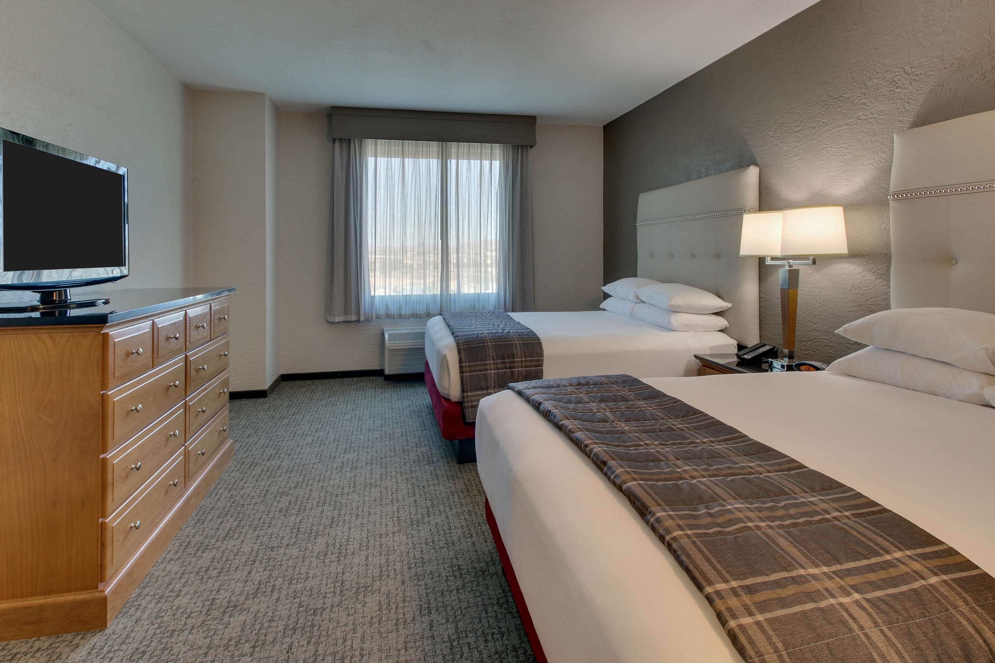 A hotel room with two beds, a television, a dresser, a lamp, and a window with curtains.