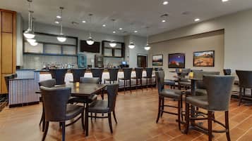 A modern dining area with multiple tables and chairs, a kitchen in the background, and artwork on the walls.