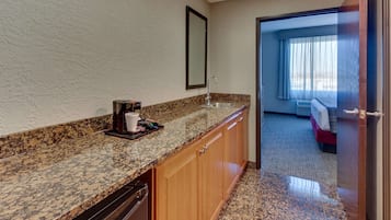 A hotel room with a kitchen area featuring granite countertops, wooden cabinets, and a stainless steel sink.
