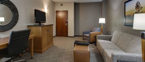 Una habitación de hotel con escritorio, televisión, sofá, sillón y lámpara.