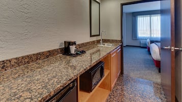 Baño de hotel con encimera de granito, lavabo, espejo, microondas y cafetera.