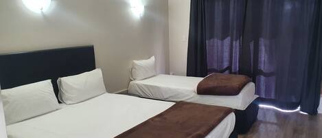 A hotel room with two beds, a ceiling light, an air conditioning unit, and a window with curtains.