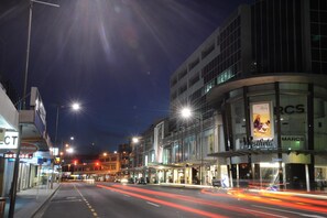 Vista nocturna de una calle con un edificio que muestra un cartel de 'Marcs' y un cartel de 'Westfield'.