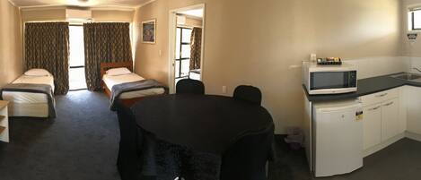Een hotelkamer met twee bedden, een bureau met telefoon, een televisie, een kitchenette met magnetron en kookplaat, en een raam met gordijnen.