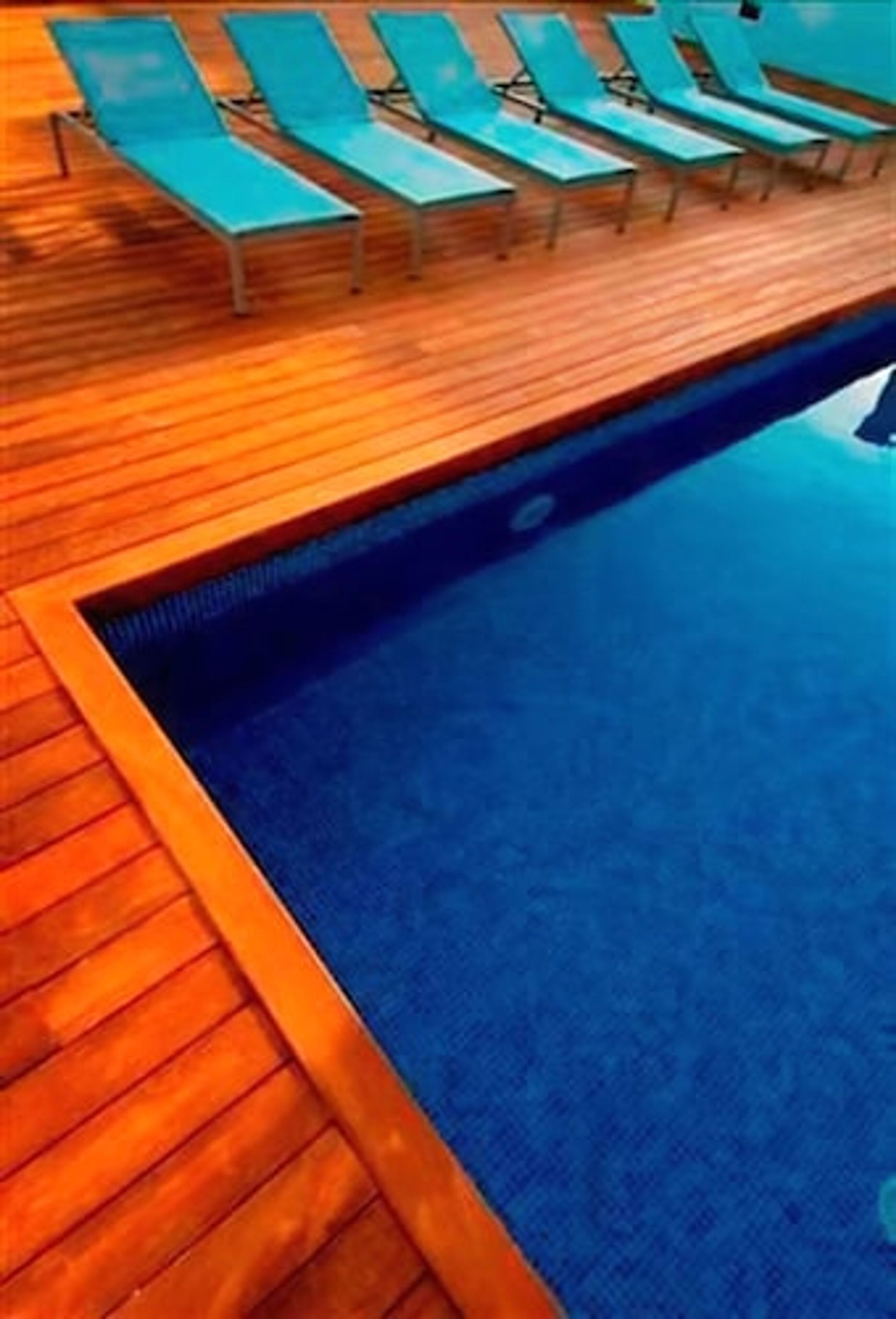 A pool area with wooden decking and lounge chairs.