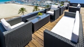 A balcony with wicker furniture, a view of a marina, and a beach. - Nautic Hotel & Spa (Palma de Mallorca)