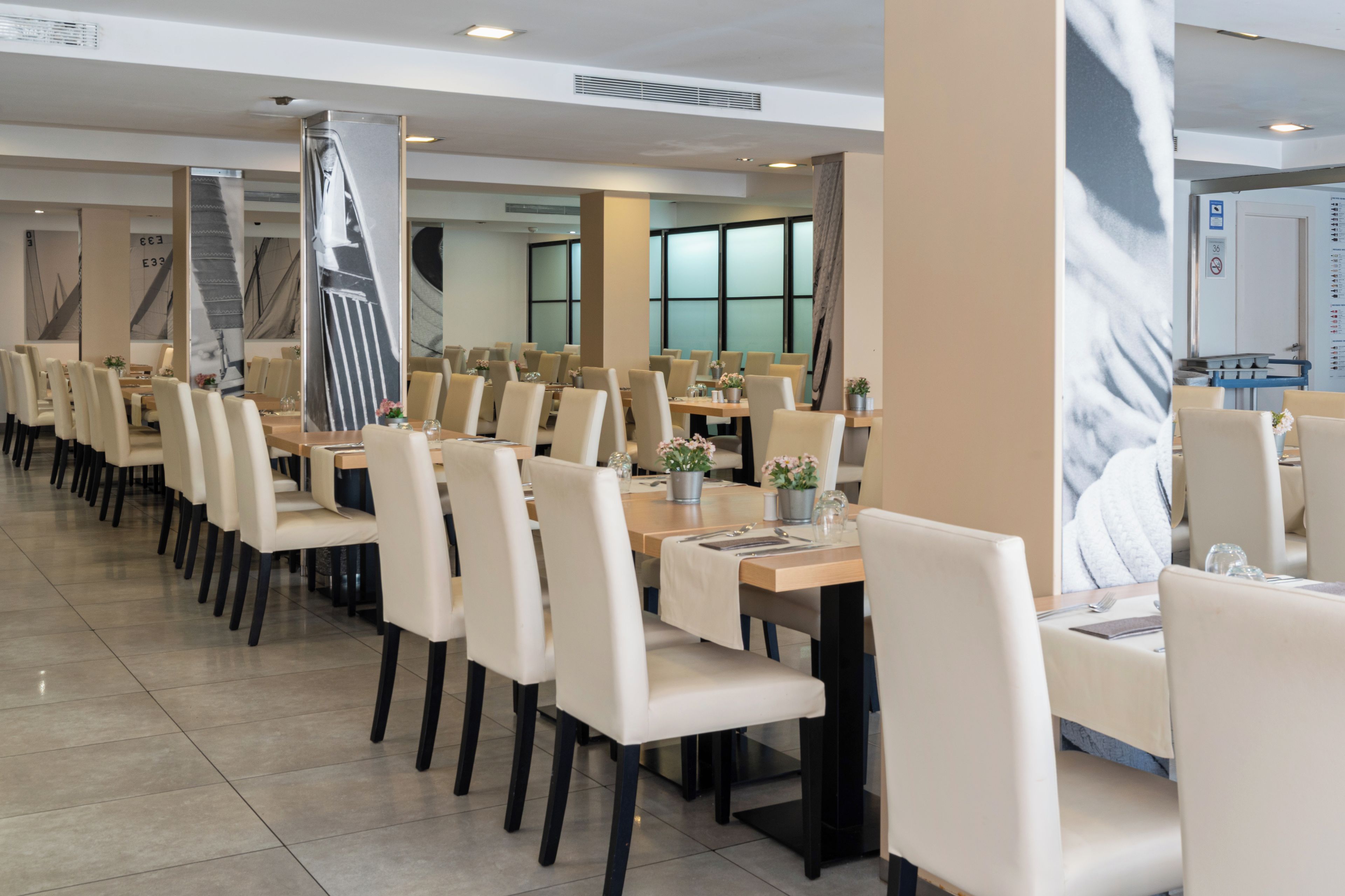 Un espace de restauration moderne, doté de longues tables et de chaises, de grandes fenêtres et d’un aménagement épuré et minimaliste.