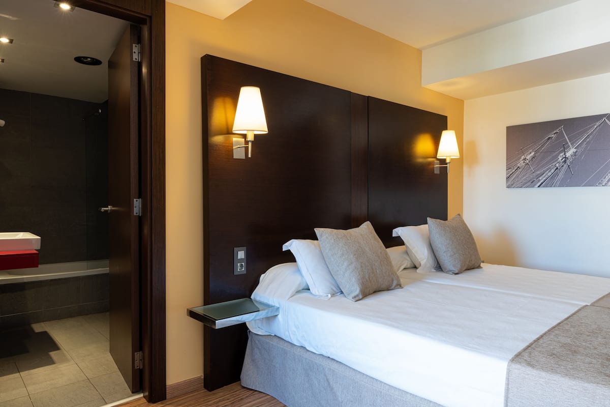 Een hotelkamer met een groot bed, twee bedlampen, een nachtkastje en een badkamer zichtbaar door een geopende deur.