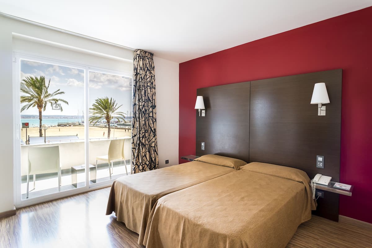 Een hotelkamer met twee bedden, een balkon met uitzicht op het strand en een rode accentmuur.