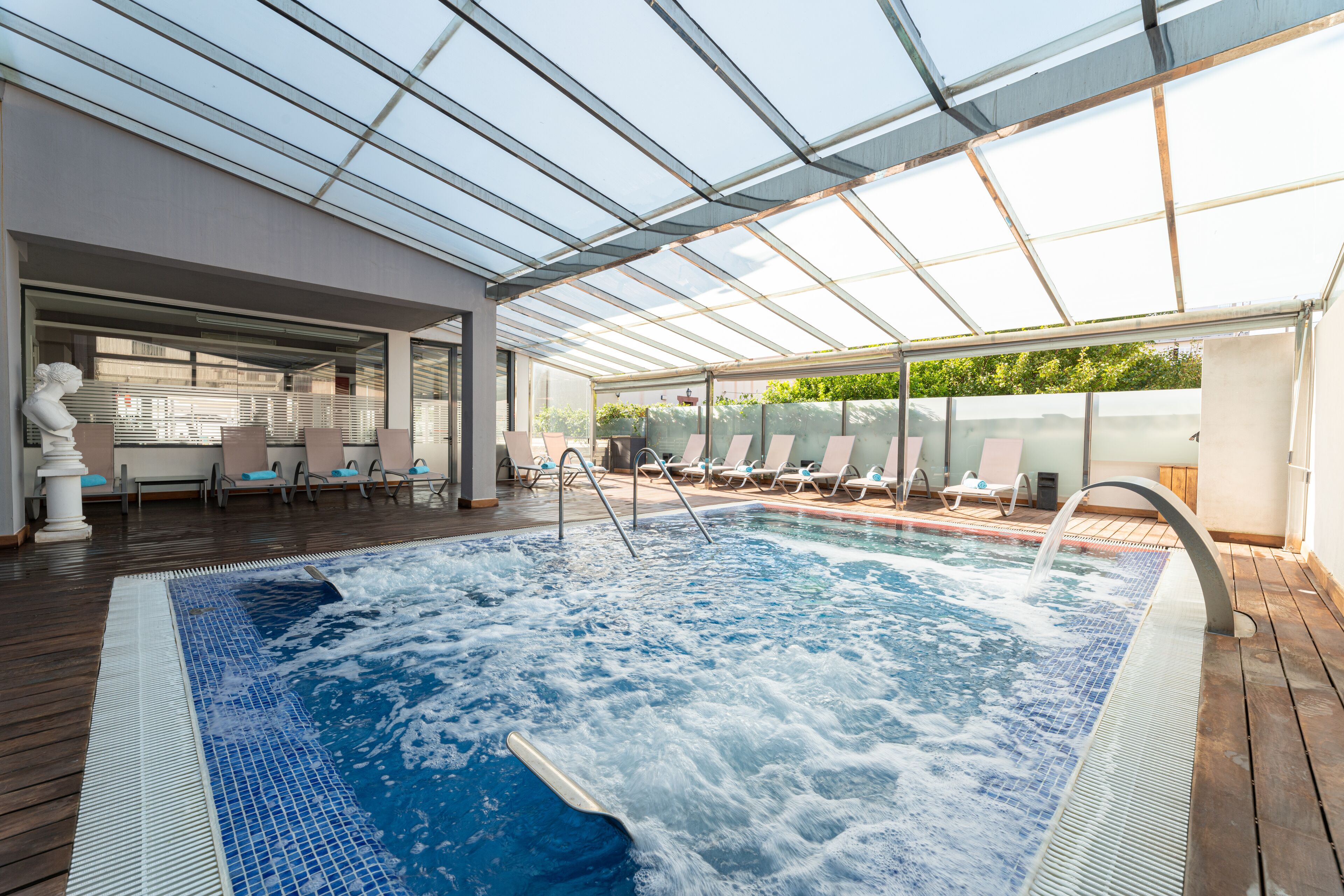 A rooftop pool area with a glass ceiling, lounge chairs, and a hot tub.
