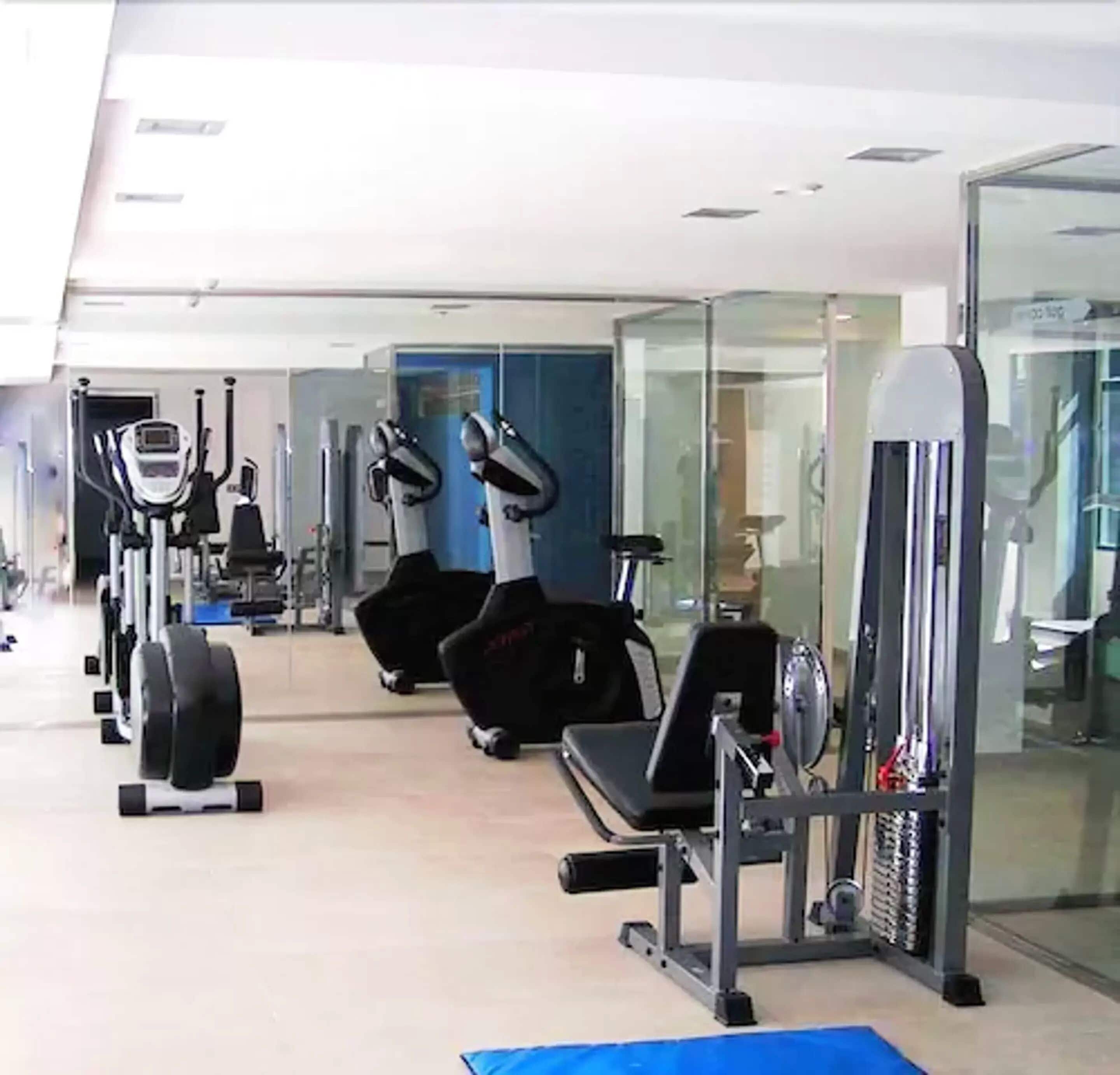 Une salle de sport équipée de divers appareils d’exercice, notamment des tapis de course, des vélos d’appartement et des appareils de musculation.