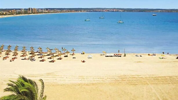 A beach with rows of sun umbrellas and beach chairs, a sandy shore, and boats in the water. - Nautic Hotel & Spa (Palma de Mallorca)
