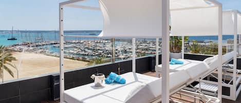 Un balcón con sillones blancos y vista a un puerto deportivo y una playa.