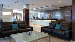 A modern living area with two leather sofas, a glass coffee table, and a reception desk in the background. - Nautic Hotel & Spa (Palma de Mallorca)