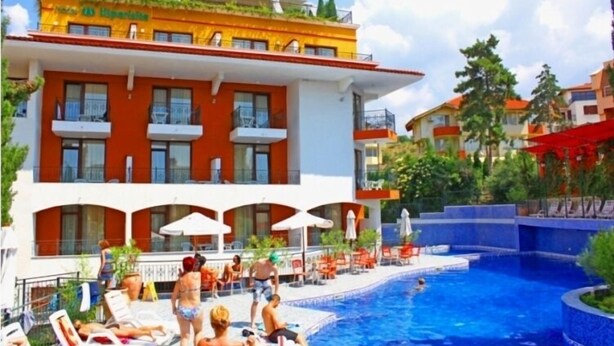 Un hotel con piscina, zona de estar al aire libre y fachada roja y blanca.