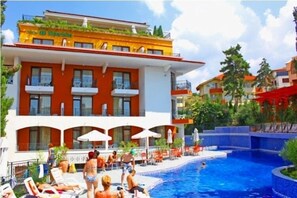 Un hotel con piscina, zona de estar al aire libre y fachada roja y blanca.