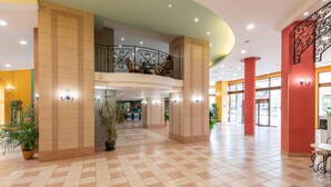 Eine geräumige Lobby mit Schachbrettmuster-Boden, ein zweistöckiger Balkon mit aufwendiger Geländerarbeiten und große Säulen.
