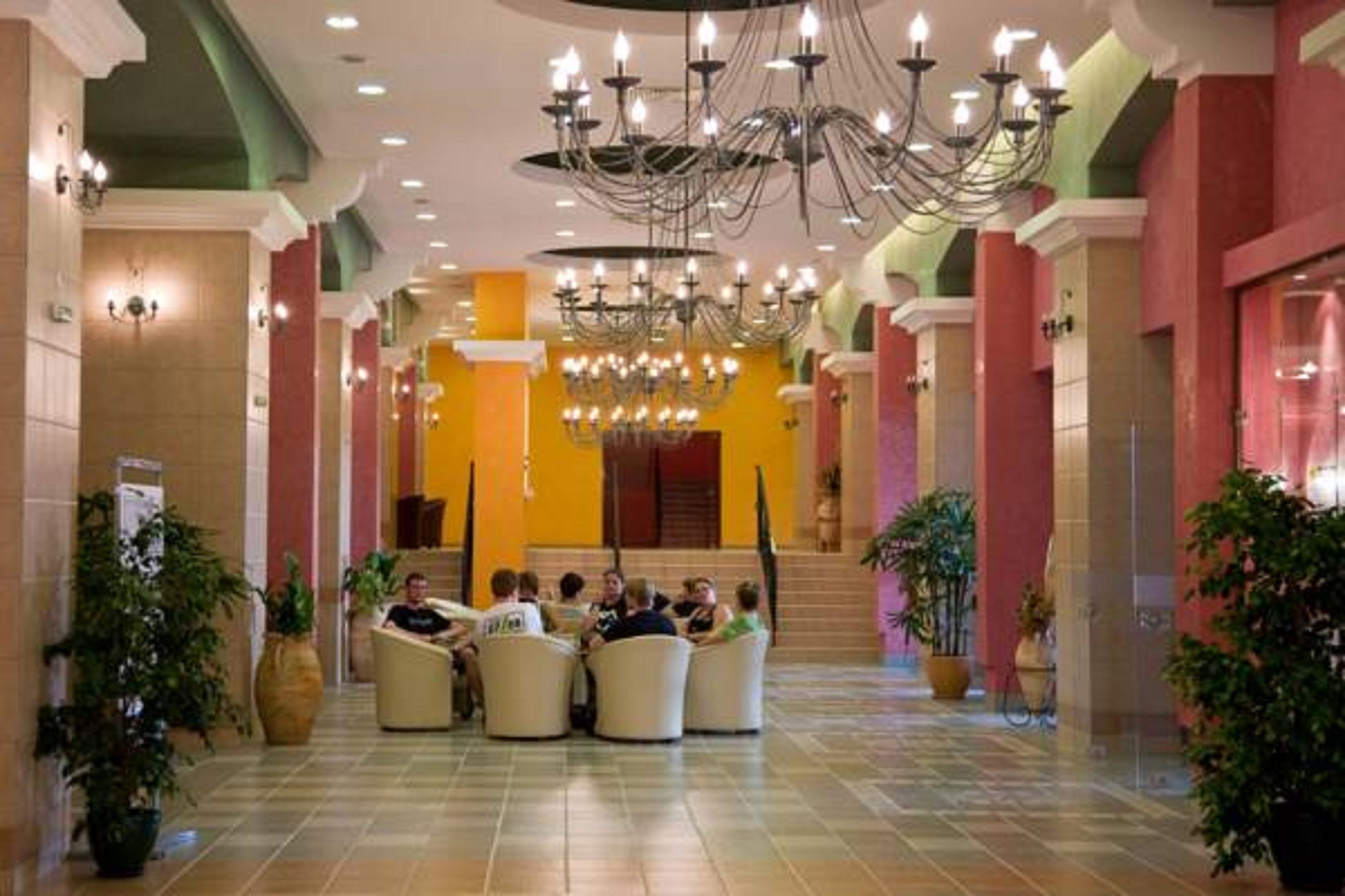 Un vestíbulo de hotel con una zona de estar central, varios candelabros y plantas en macetas.