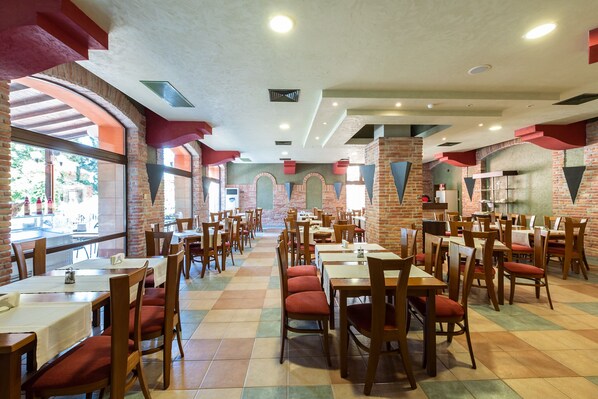 A spacious restaurant with multiple dining tables and chairs, brick walls, and large windows allowing natural light.