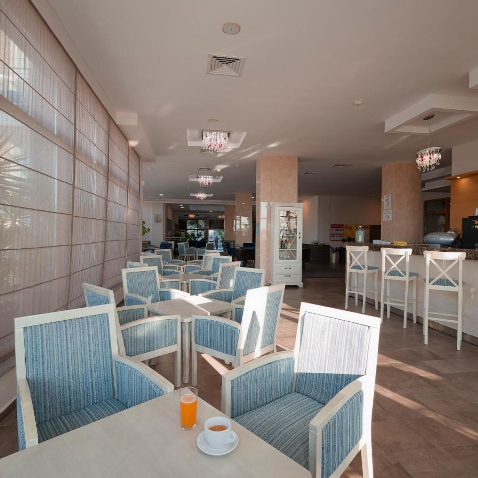 A hotel dining area with multiple tables and chairs, a bar area, and a view of the lobby.