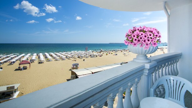 Varanda com vista para a praia, um vaso de flores e área com guarda-sóis de praia.