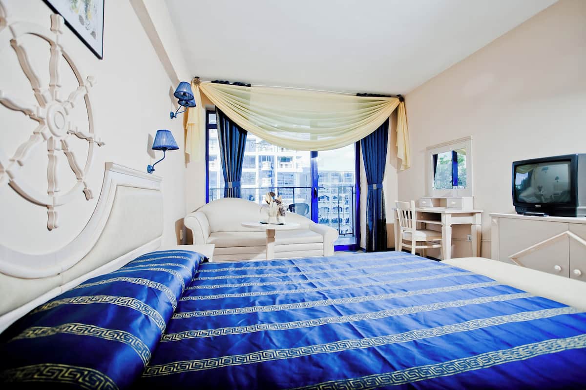 Habitación de hotel con cama, escritorio, silla, televisión y vistas a la ciudad.