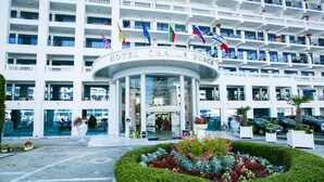 Hotel com várias varandas, entrada central e área de jardim ajardinado.