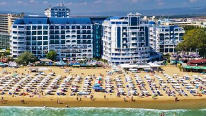 Um hotel com vários andares, uma praia com muitos guarda-sóis e vista para o mar.