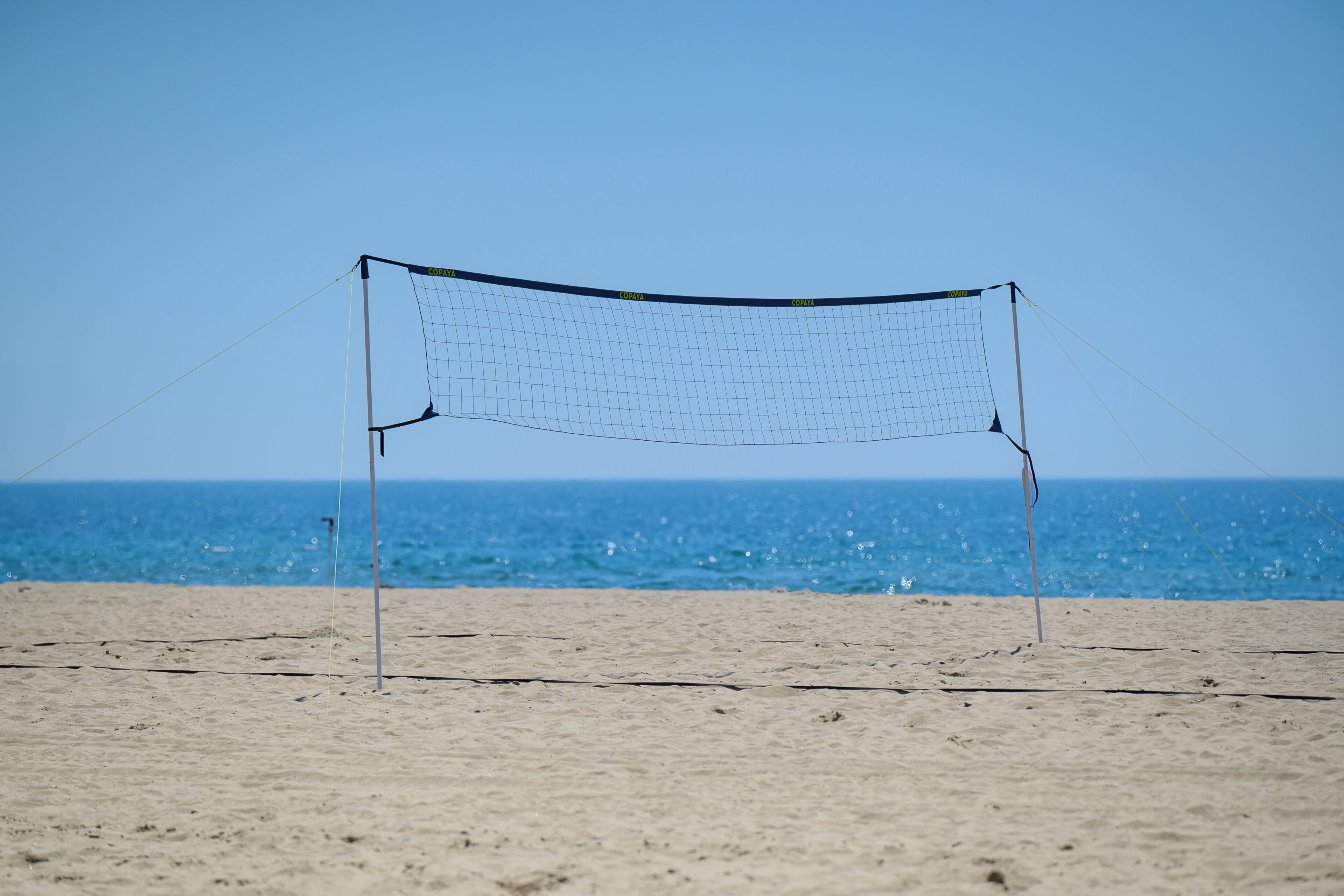 A beach volleyball net with a clear view of the ocean in the background.