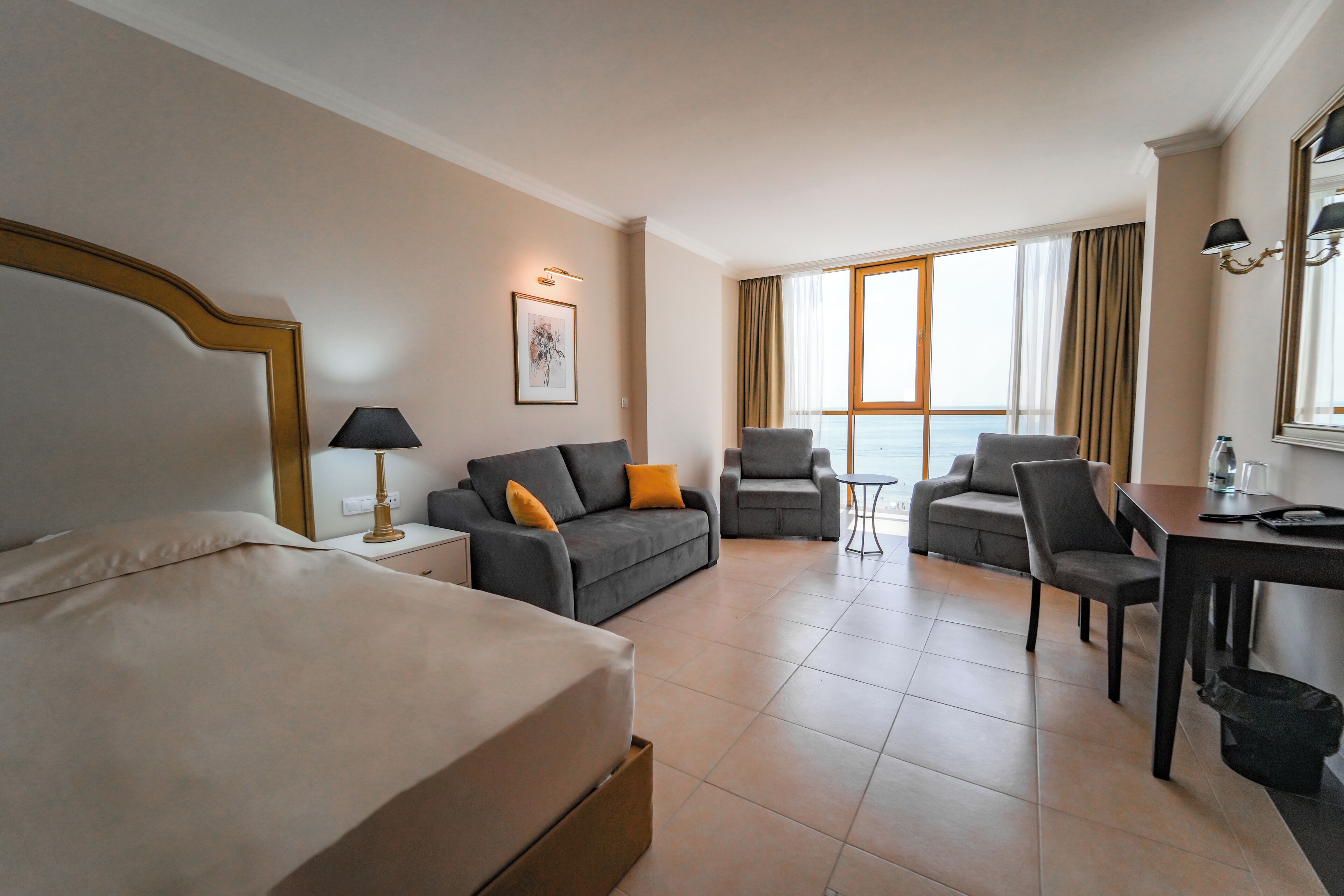 A hotel room with a bed, two armchairs, a sofa, a desk, and a window with curtains.