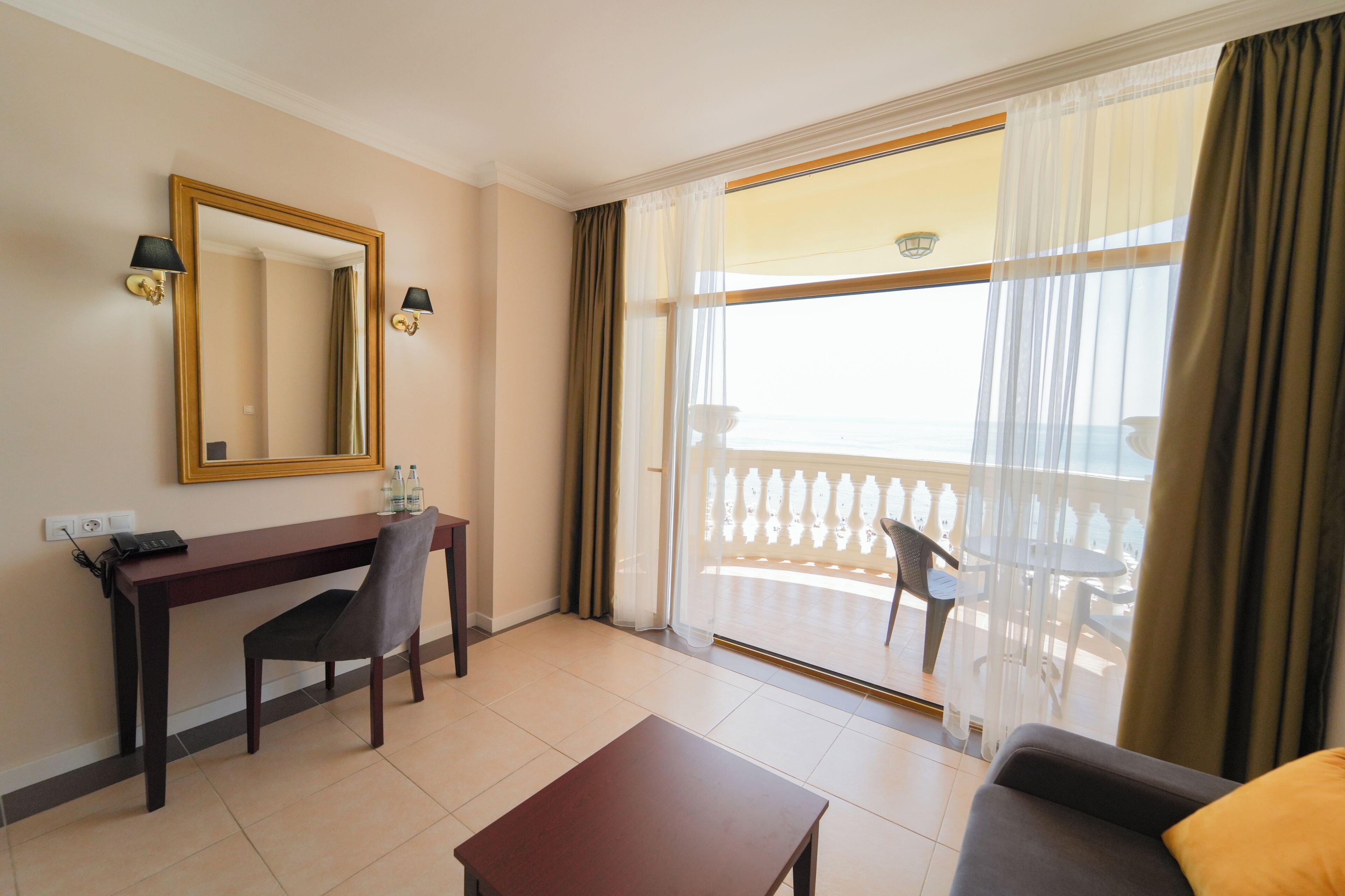 A hotel room with a desk, chair, and a sofa. There is a balcony with a view.