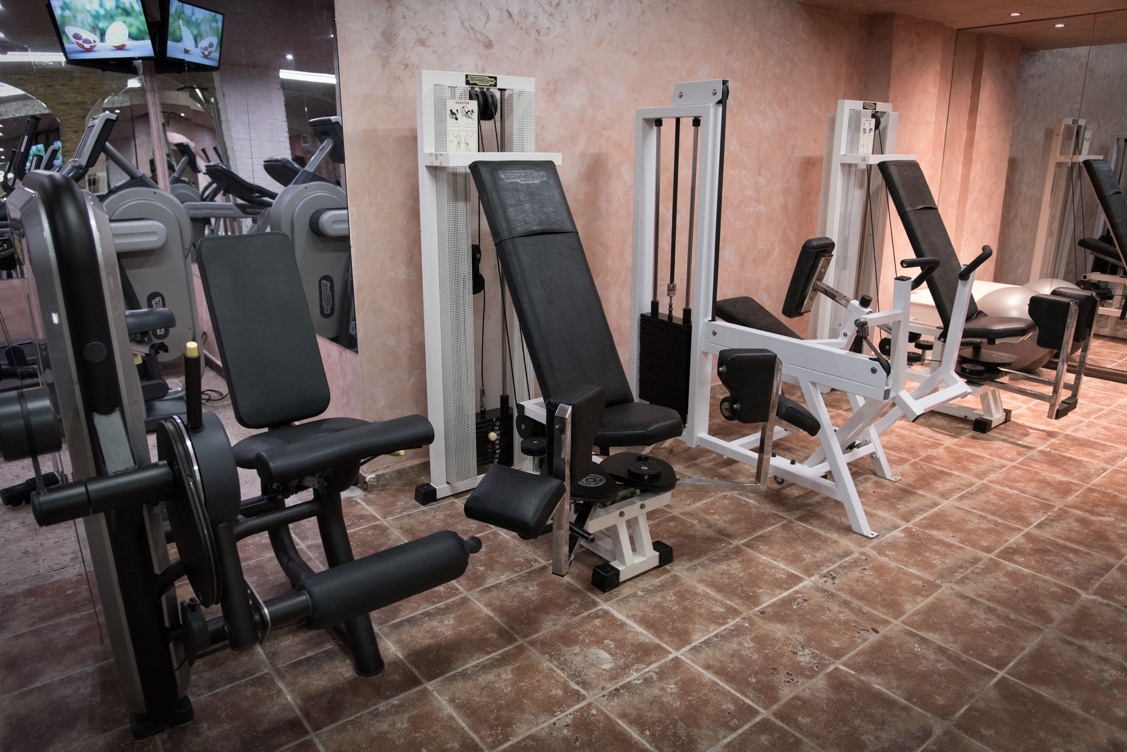 Une salle de sport équipée de divers appareils d’exercice, notamment des bancs de musculation et des appareils de cardio.
