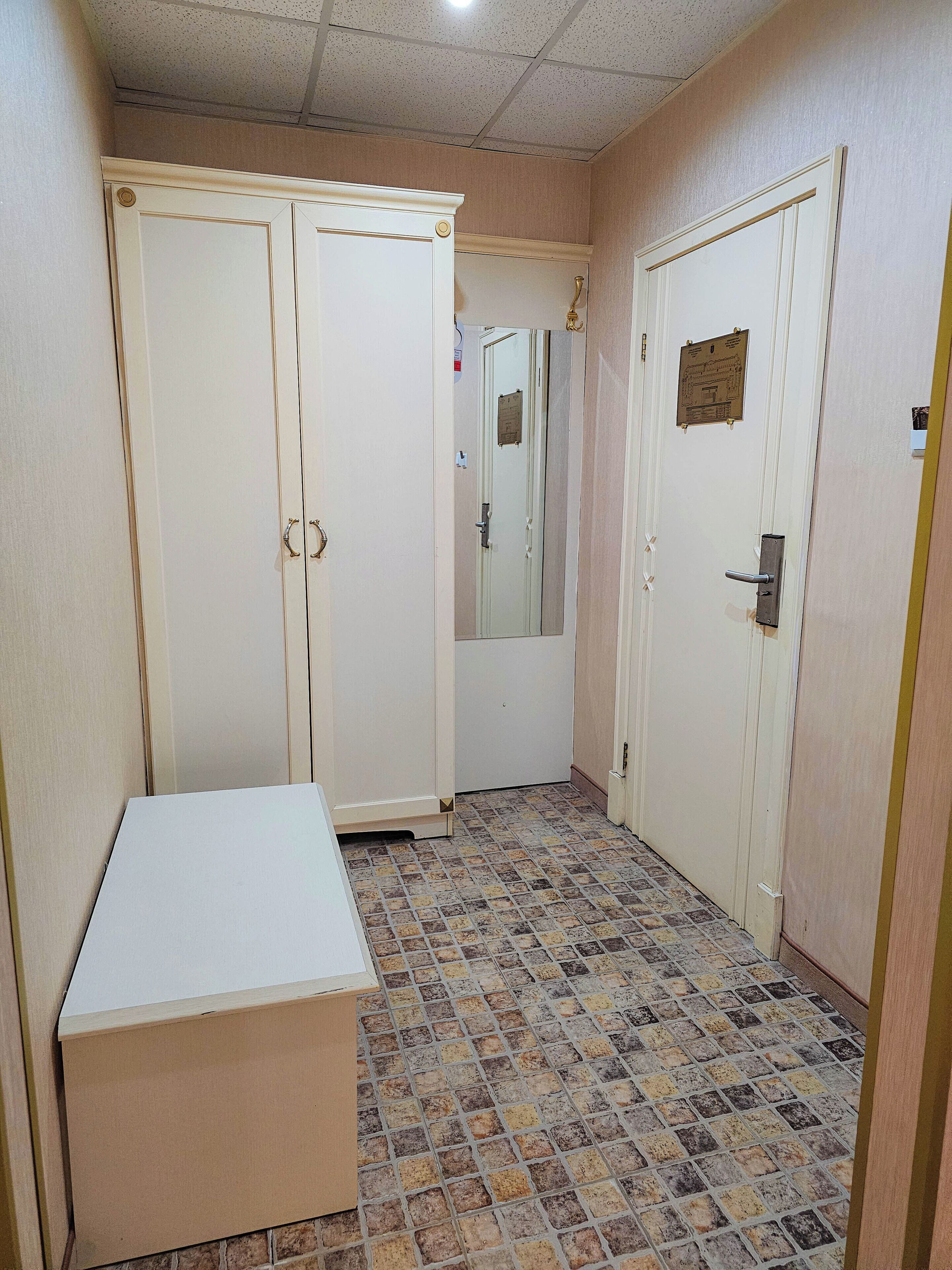 A hallway with a white wardrobe, a door with a plaque, and a tiled floor.