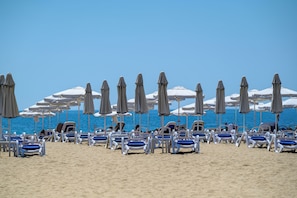 A beach with rows of sun loungers and umbrellas, a clear sky, and the ocean in the background. - Imperial Palace Hotel - All Inclusive (Sunny Beach)