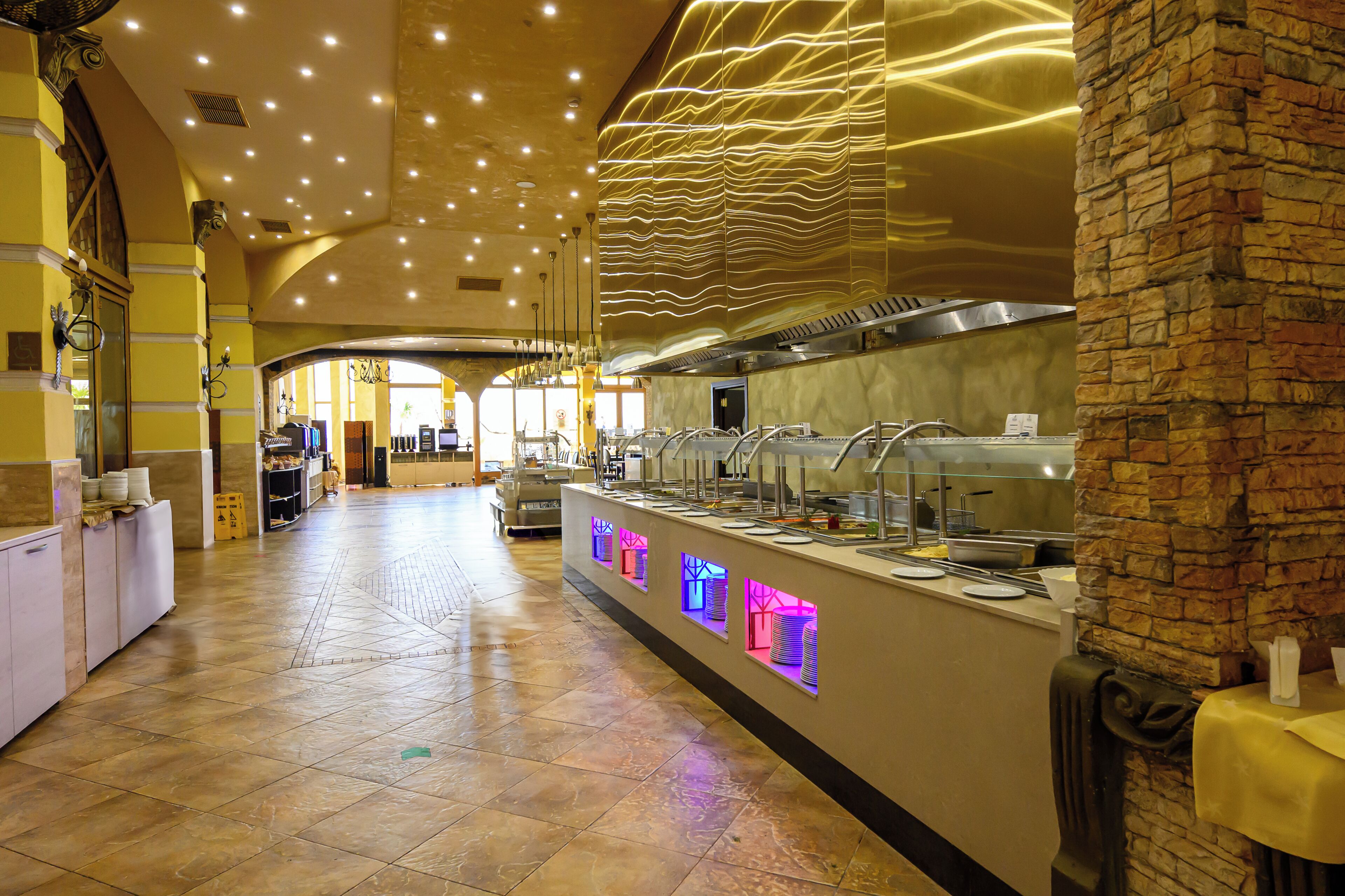 A hotel buffet area with a long counter, multiple serving stations, and a tiled floor.