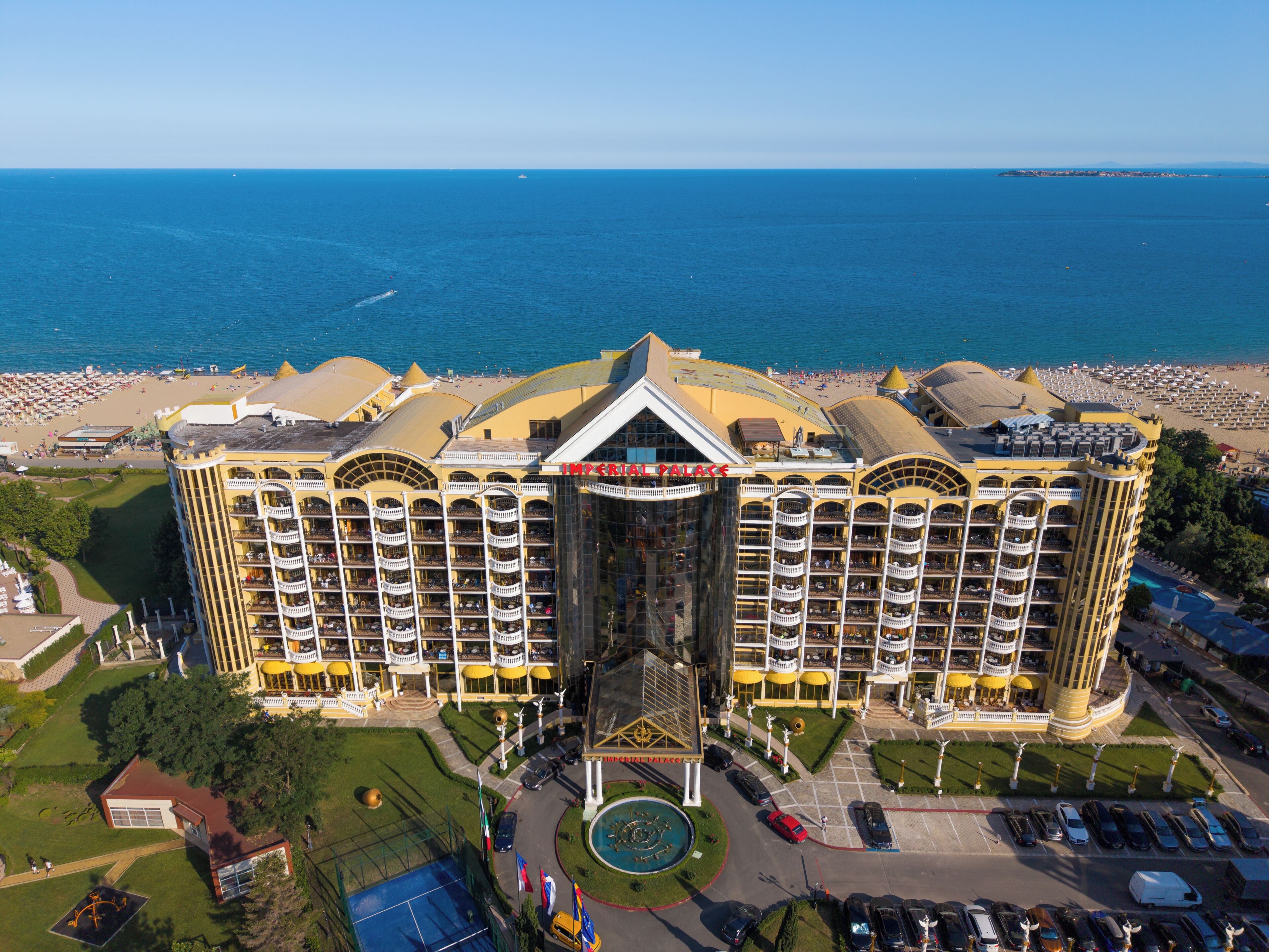 Un hotel grande con múltiples balcones, un patio central y vista a la playa.