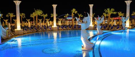 Una piscina con estatuas de ángeles, palmeras y sillas de descanso.