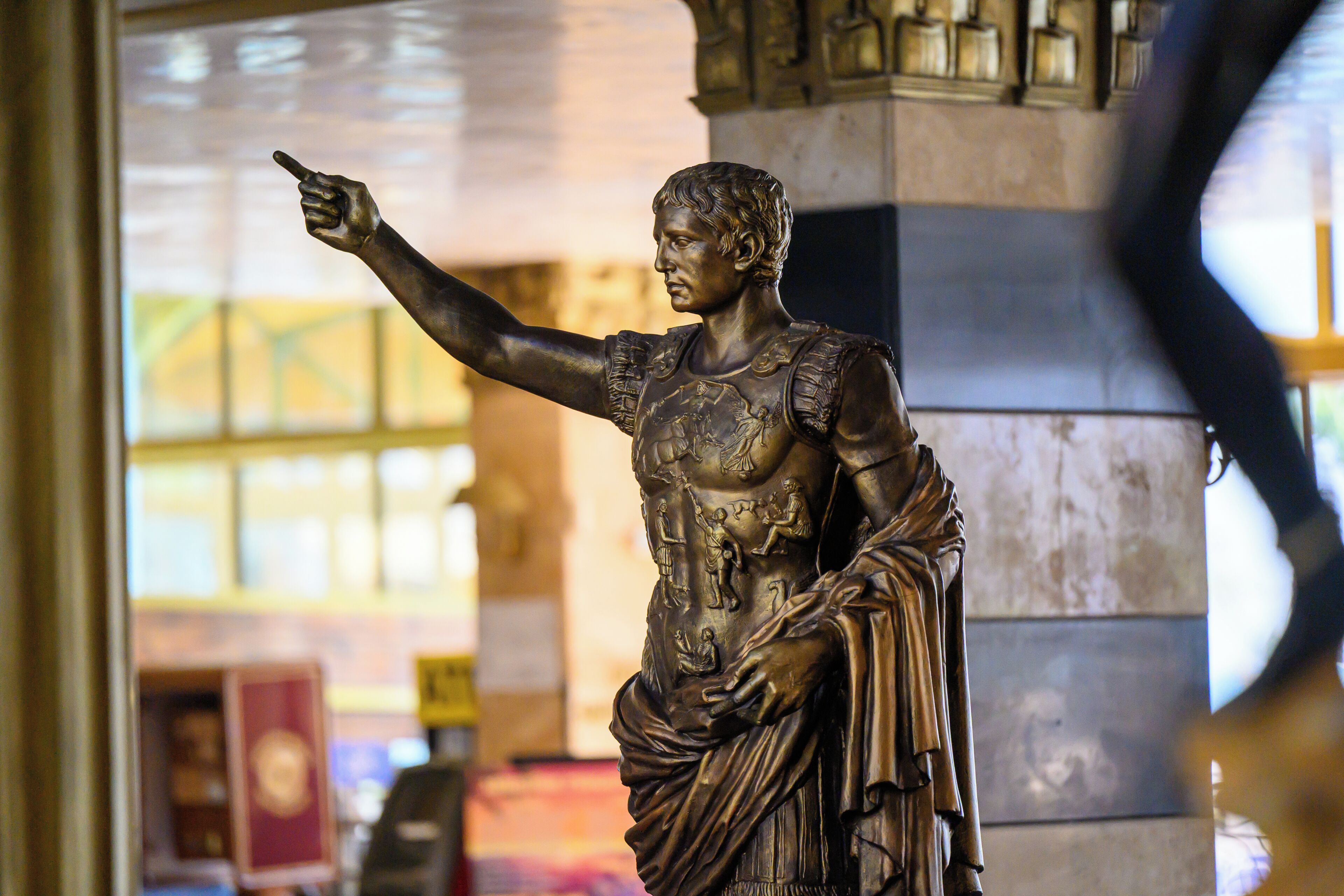 A statue with a pointing gesture, set against a backdrop of architectural columns and a window.