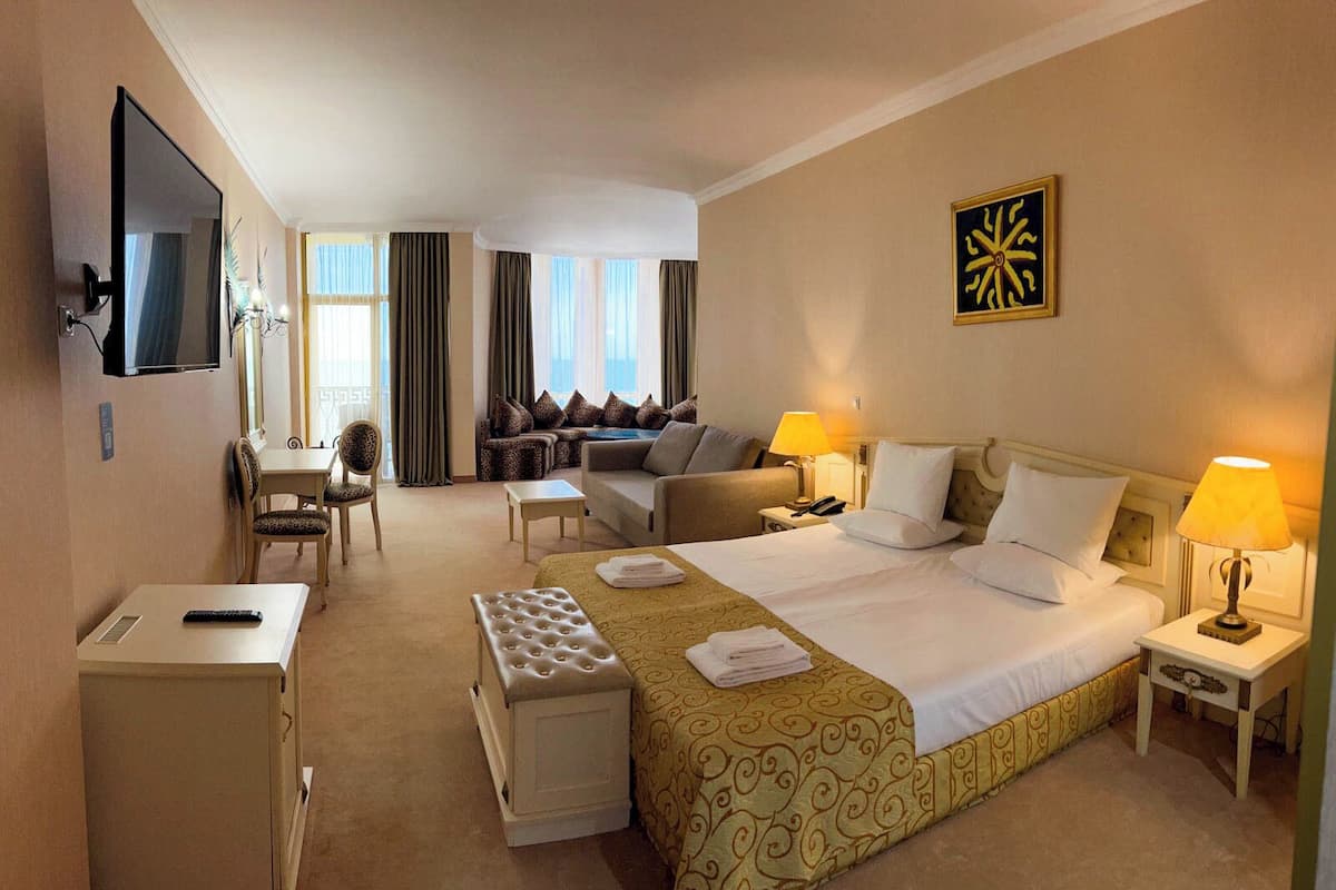 A hotel room with a large bed, a desk, a chair, a sofa, and a TV.