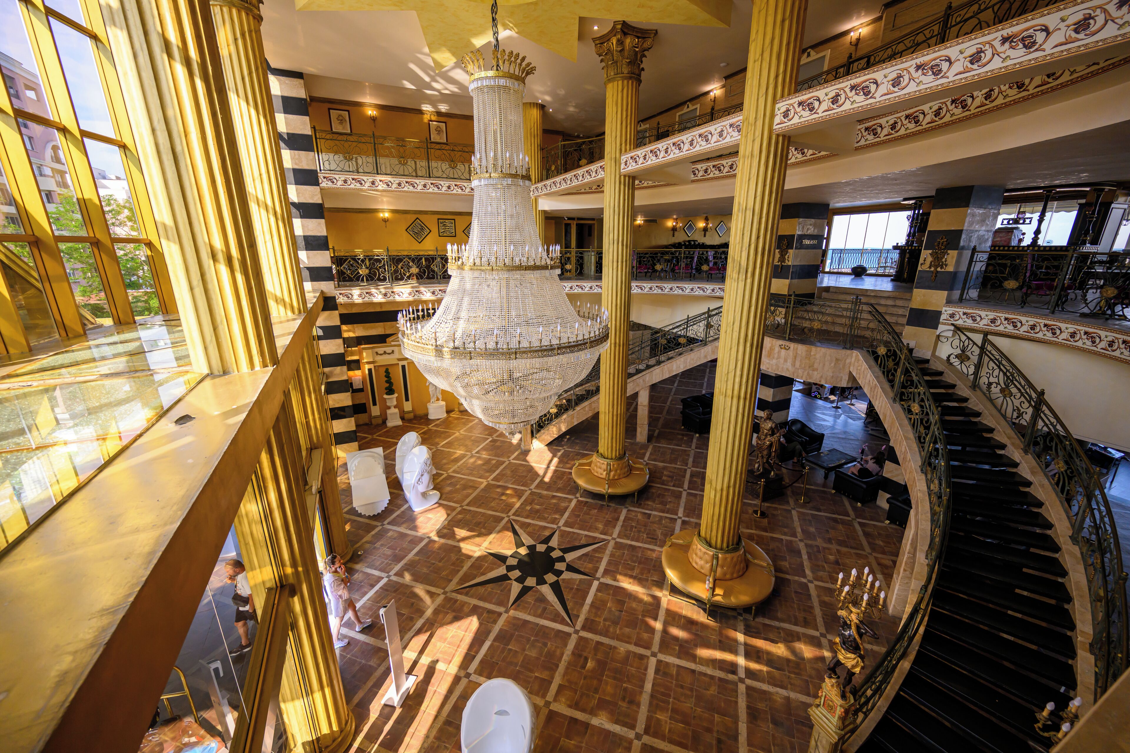 A multi-level atrium with a grand chandelier, ornate railings, and a checkered floor pattern.