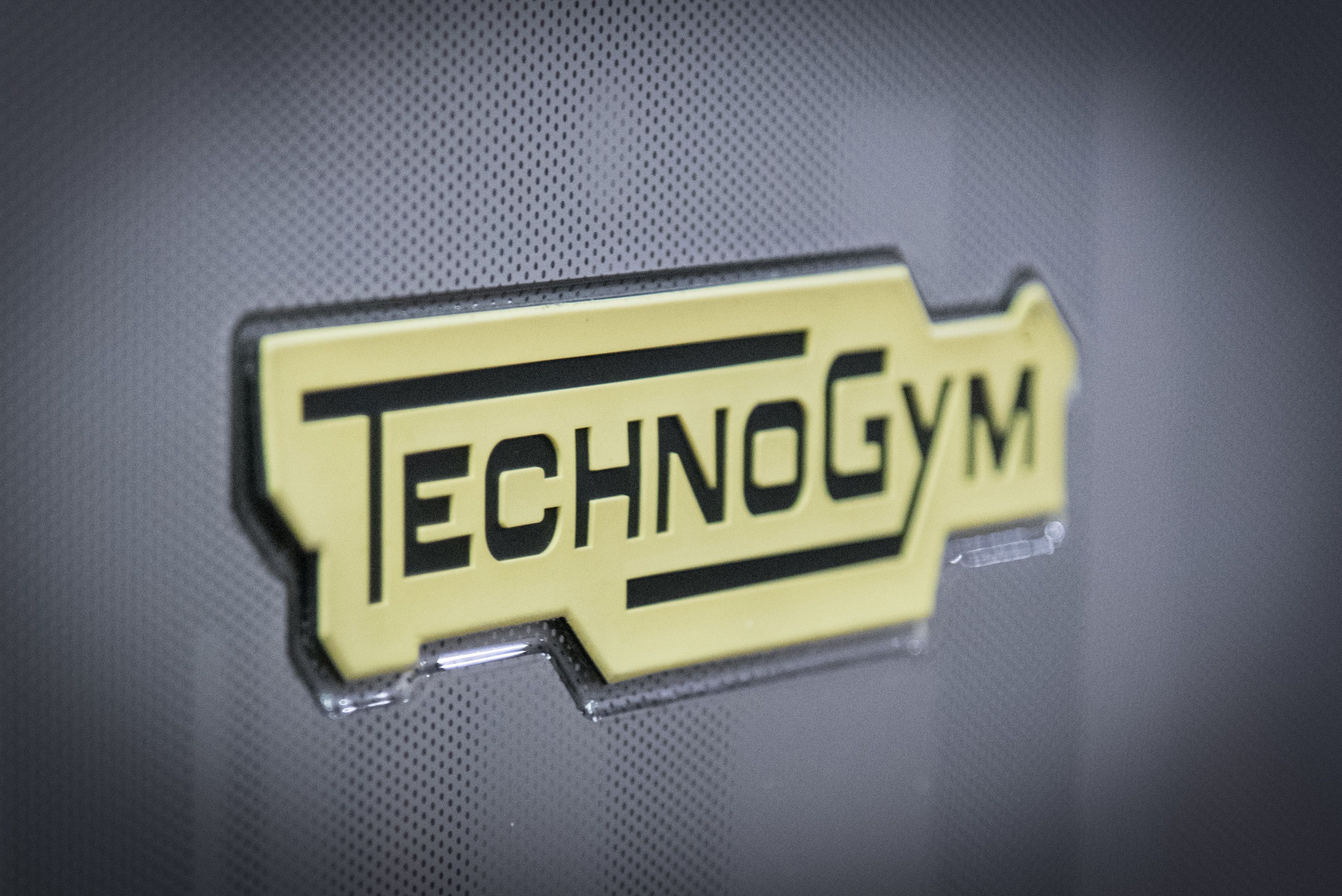 A yellow sign with the text "TechnoGym" on a textured surface.