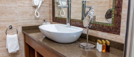 Un baño con un lavamanos blanco grande, un espejo y un perchero. Hay artículos de aseo en la encimera.