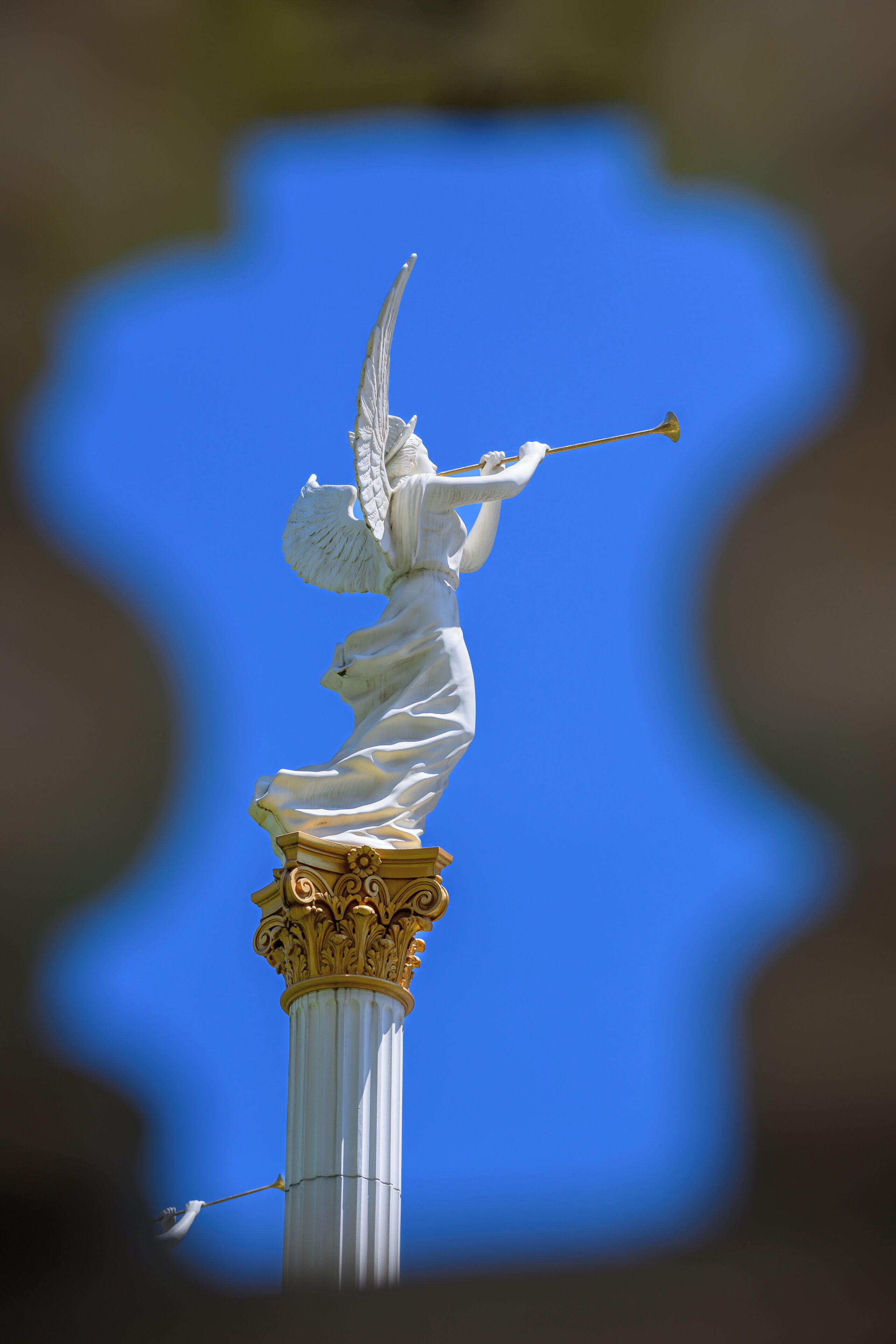 A statue of an angel with outstretched wings and a trumpet, mounted on a column with ornate capitals.