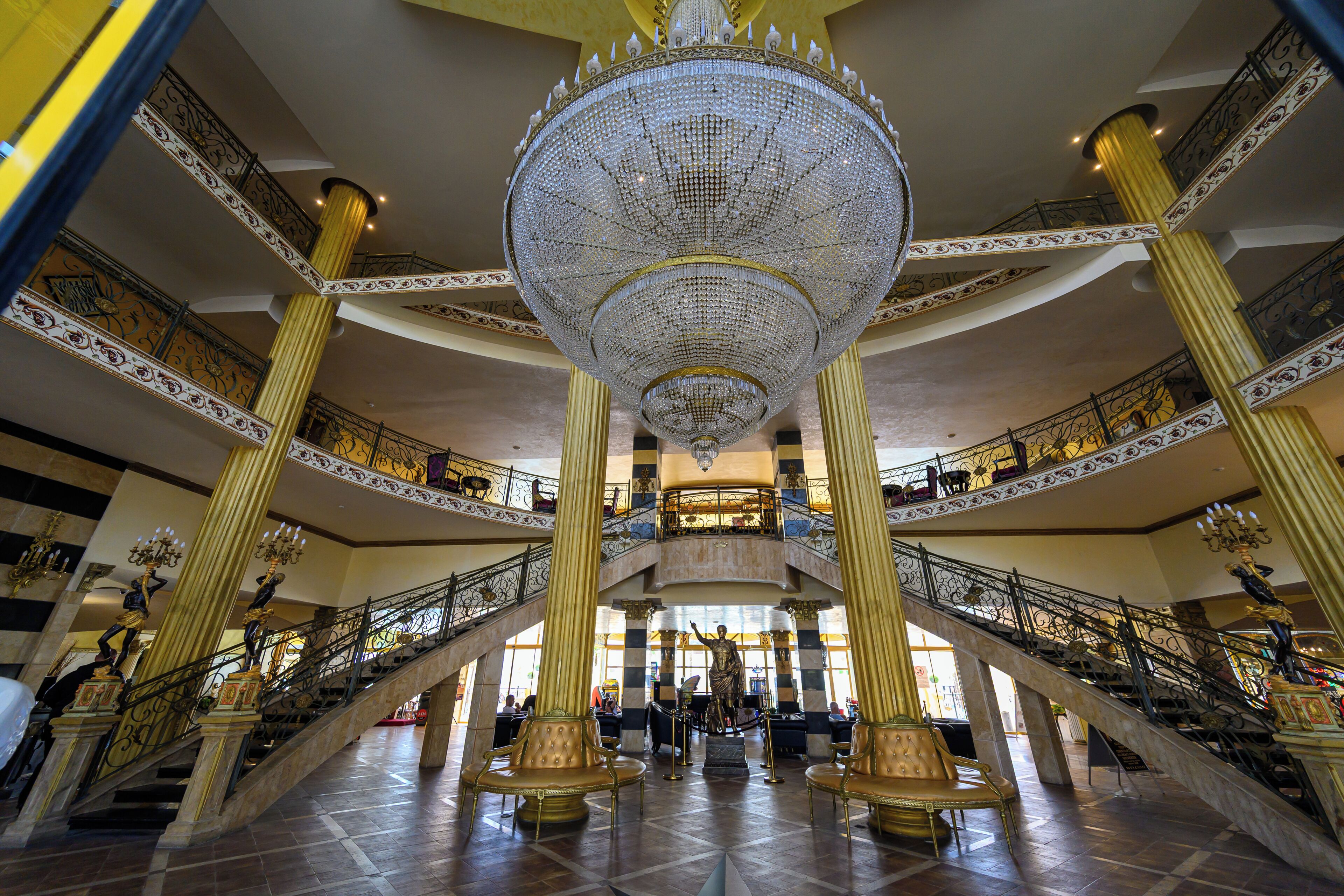 A grand interior with a large chandelier, ornate columns, and a central staircase.