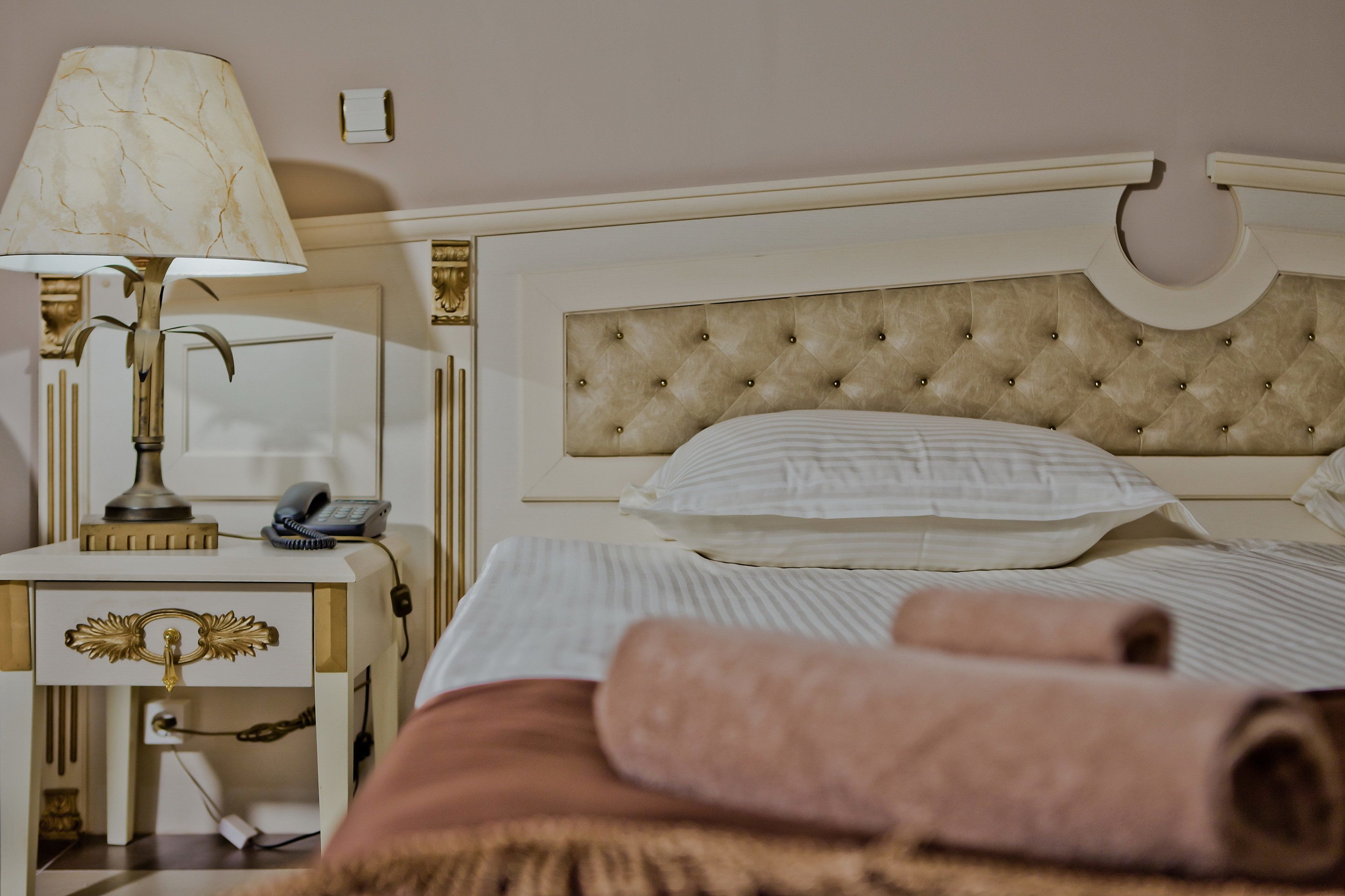 Una cama bien hecha con sábanas blancas, un cabecero color beige y una lámpara de noche.